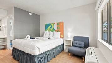 A hotel room with a bed, a chair, a bedside table, a lamp, and a window.