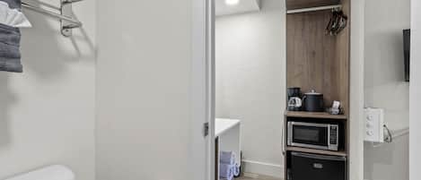 A compact bathroom with a toilet, a towel rack, a shelf with towels, a microwave, and a refrigerator.