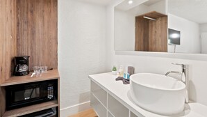 A modern bathroom with a white sink, a large mirror, a wooden shelf with a coffee maker, and a microwave. - Budget Disney Room Pool & Parking (Kissimmee)