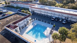 An aerial view of a hotel with a swimming pool, parking area, and adjacent buildings. - Budget Disney Room Pool & Parking (Kissimmee)