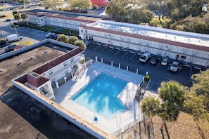 Vista aérea de un hotel con piscina, zona de estacionamiento y edificios adyacentes.