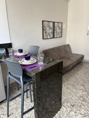 Un comedor con una mesa dispuesta para dos personas, una silla gris, un sofá gris y una pared con dos obras de arte abstracto.