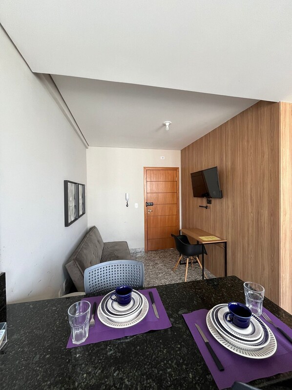 A compact living space with a kitchenette, a dining area, a sofa, and a television mounted on the wall. - LK Lourdes 12 (Belo Horizonte)