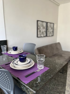 Een eettafel gedekt met borden, kommen en glazen, een stoel en een bank in een kamer met kunst aan de muur.