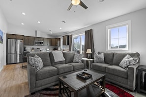 A modern living room with a grey sofa set, a coffee table, and a kitchen in the background.