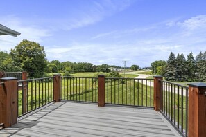 A wooden deck with a metal railing overlooking a grassy area and a road.