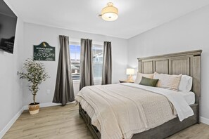 A bedroom with a bed, curtains, a potted plant, a wall-mounted sign, and a ceiling light fixture.