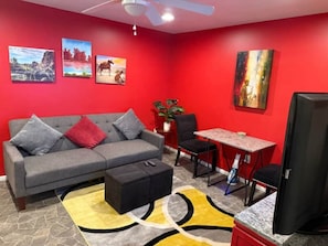 Ein Wohnzimmer mit grauem Sofa, schwarzem Hocker, roten Wänden und einem Essbereich mit Tisch und Stühlen.