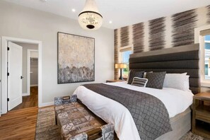 Un dormitorio con una cama grande, una araña, una obra de arte en la pared y un banco estampado.