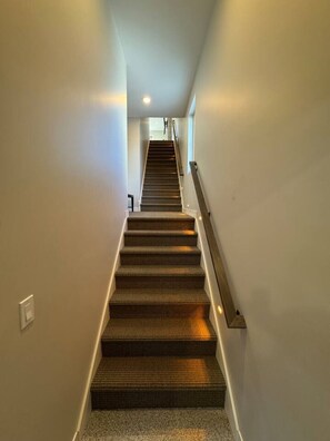 Una escalera con peldaños alfombrados y barandilla, que conduce a una plataforma con una lámpara.