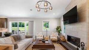 A living room with a sofa, chairs, a coffee table, a fireplace, and a TV mounted on the wall.