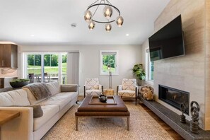 A living room with a sofa, chairs, a coffee table, a fireplace, and a TV mounted on the wall.