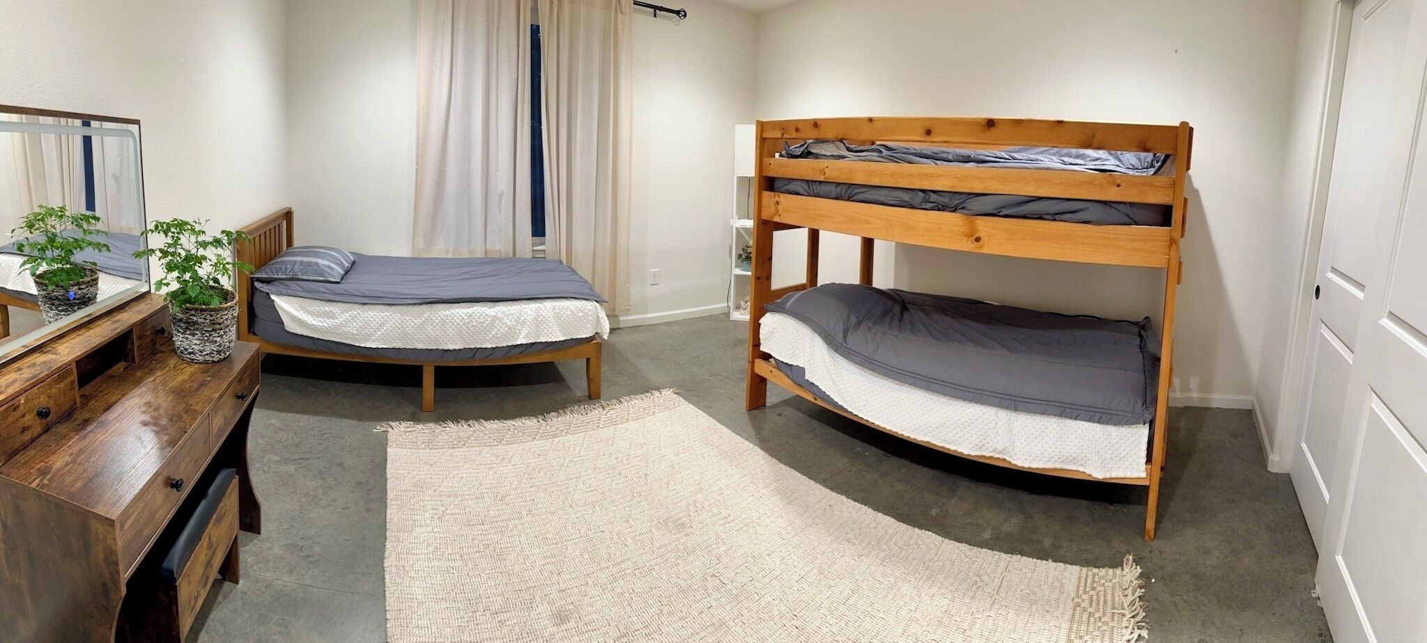 Une chambre avec deux lits superposés, un bureau en bois, un miroir, une plante et une fenêtre avec des rideaux.