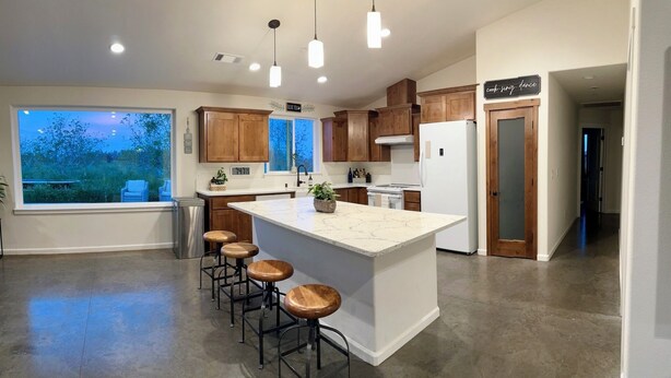 A modern kitchen with wooden cabinets, a large island with stools, and pendant lighting. - HandyFarms.com: California Organic Farm Stay on a Red Walnut Orchard Nut Store (Corning)