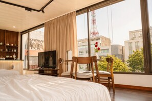 A hotel room with a large bed, a television, a wooden cabinet with dishes, and a view of buildings and a tower outside. - Cozy Old Quarter Retreat Walk to Hoan Kiem Lake & Major Landmarks (Hà Nội)