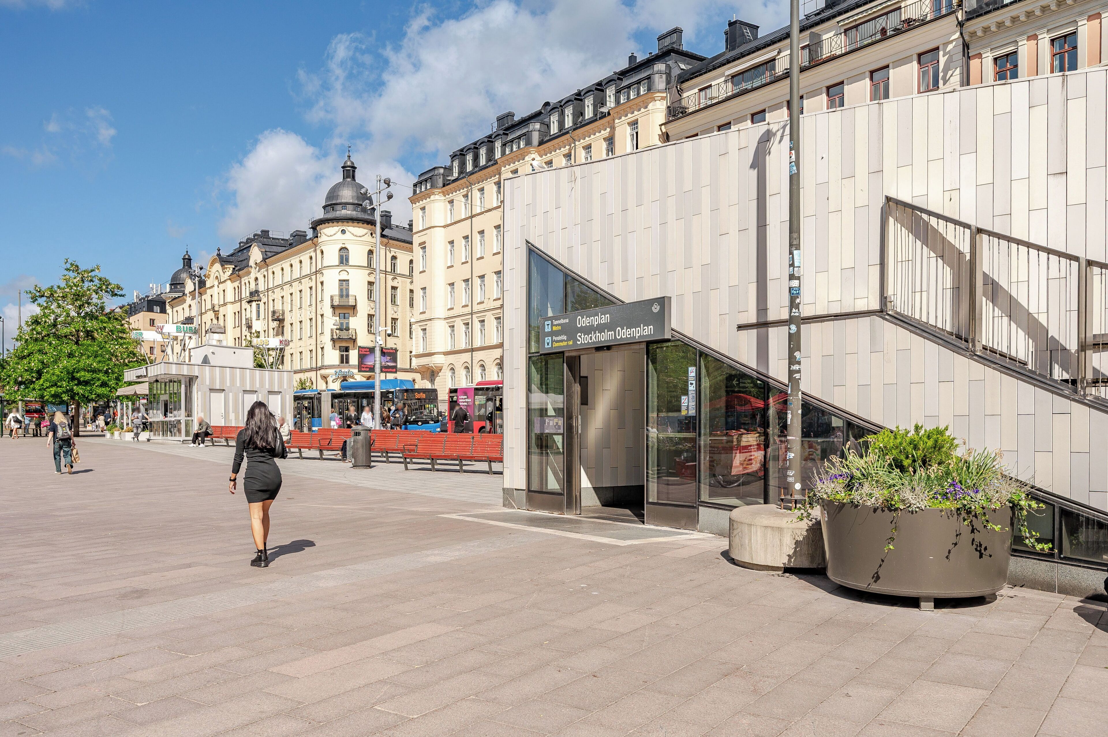 A public square with a modern building, a tram, and a woman walking.