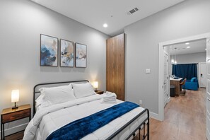 Moderni hotellihuone, jossa on sänky, yöpöydät, vaatekaappi ja näkymä oleskelutilaan.