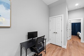 A room with a desk, a computer, a chair, a door, and a bed with a blue curtain. - New Elegant Apt+Free Parking+Fireplace+Stockyards (Fort Worth)