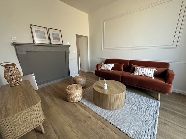 A living room with a sofa, two wicker side tables, a round wooden coffee table, a fireplace, and a patterned rug.