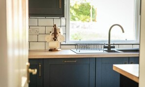 Una cocina con armarios oscuros, una ventana con vistas a la vegetación y un lavabo con grifo.