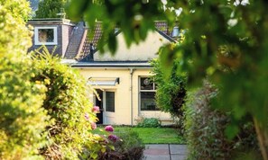 Una casa con techo inclinado, una chimenea visible y un pequeño jardín delantero con un sendero que lleva a la entrada.