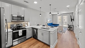 A modern kitchen with stainless steel appliances, a blue sofa, and a dining area. - New Modern King bed+Pool+Gym+Parking+Stockyards (Fort Worth)