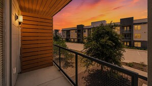 A balcony with a view of a modern building complex during sunset. - New Modern King bed+Pool+Gym+Parking+Stockyards (Fort Worth)