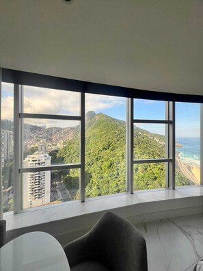 Una habitación con amplios ventanales que ofrecen vistas a un paisaje urbano, una montaña y una playa.