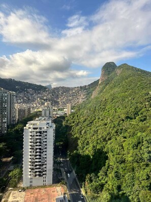 Un edificio alto con vistas a una ciudad densamente poblada y una colina verde prominente al fondo.