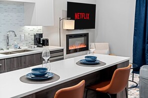 Een moderne keuken met een ingebouwde open haard, een eethoek met blauwe borden en glazen, en een televisie waarop 'NETFLIX' staat.