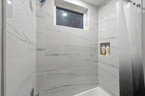 Een badkamer met marmeren wanden, een douchegordijn en een klein plankje met toiletartikelen.
