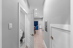 Ein Flur, der zu einem Raum mit Toilette, einem blauen Stuhl und einer Tür mit Lichtschalter führt.