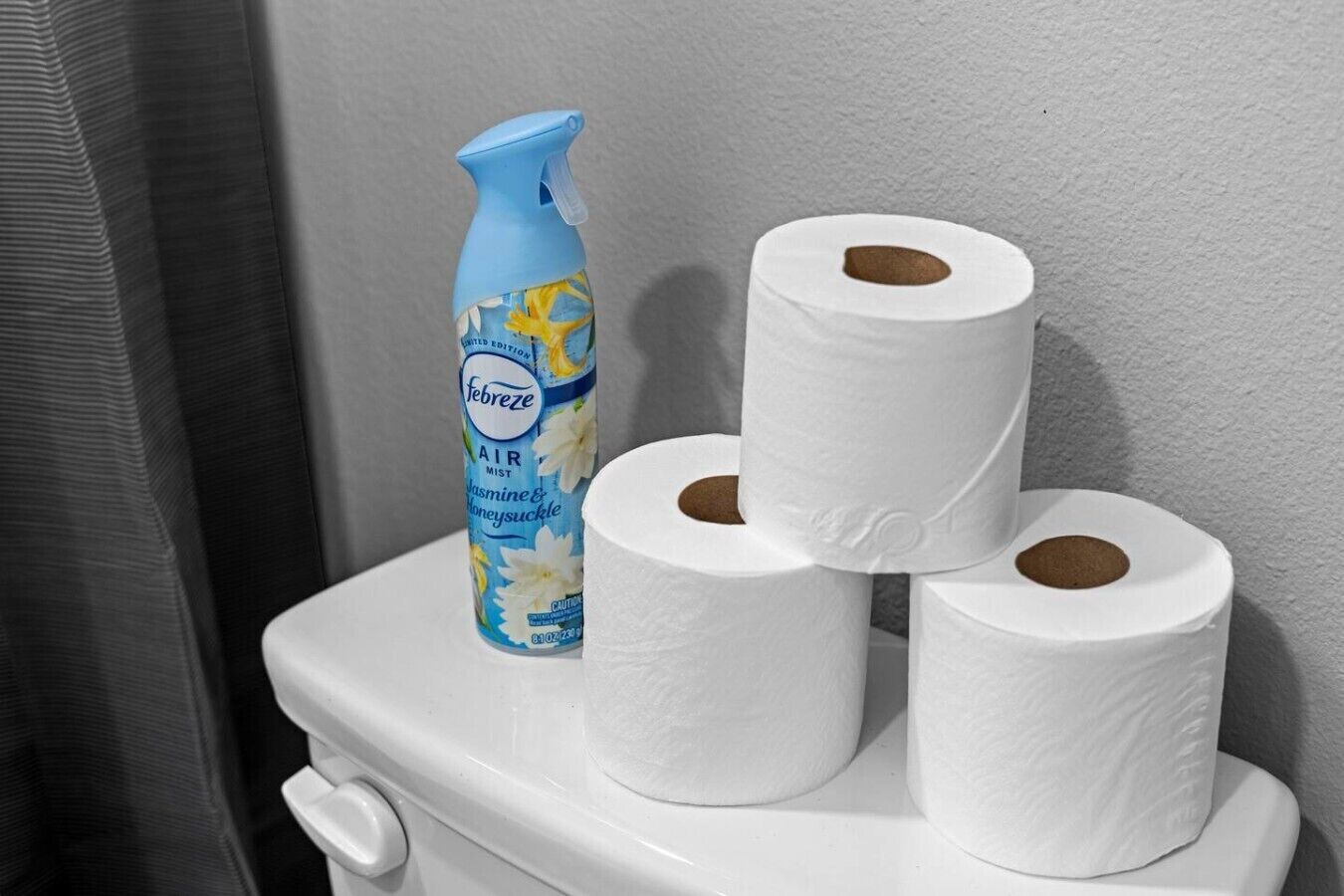 Een toilet met drie rollen toiletpapier en een fles Febreze luchtverfrisser.