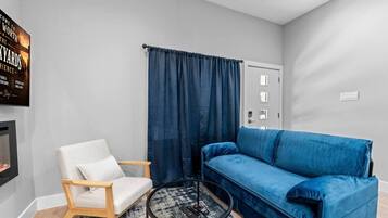 Un salon avec un fauteuil blanc, un canapé bleu, une table basse ronde et une cheminée.
