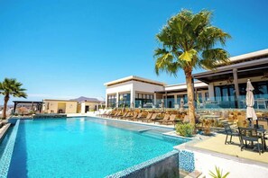 A swimming pool with lounge chairs, palm trees, and a building with large windows.