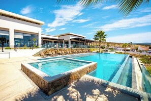 A modern hotel with a swimming pool, lounge chairs, and a view of the surrounding landscape.