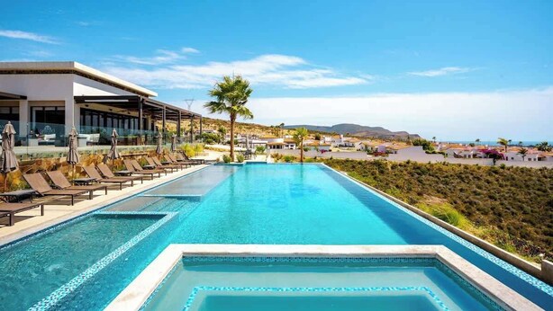 Piscina com espreguiçadeiras e vista para a área costeira.