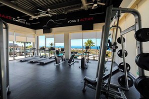 Ein Fitnessstudio mit Laufbändern, Kraftgeräten und großen Fenstern mit Meerblick.