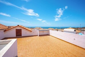 A rooftop terrace with a view of the sea, a white wall, and a tiled floor.