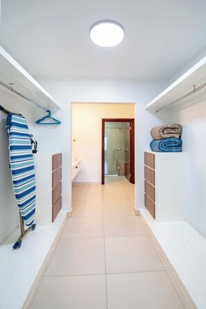 A hallway with a ceiling light, a coat rack, a folded blanket, and a door leading to a bathroom.
