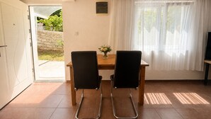 Une pièce avec une porte donnant sur un espace extérieur, une table avec deux chaises, un petit vase avec des fleurs et un téléviseur posé sur un meuble.