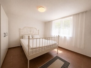A bedroom with a single bed, a wardrobe, a window with curtains, and a patterned rug.