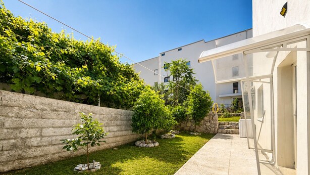 Un bâtiment moderne doté d’une cour dallée, d’un mur en pierre et d’une grande variété de plantes.