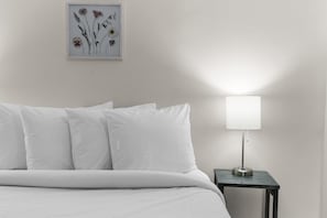 A bed with white bedding, a bedside table with a lamp, and a framed floral artwork on the wall.