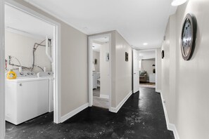 Un pasillo con lavadora, una puerta que da al baño y un reloj fijado en la pared.