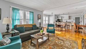A spacious living room with a sofa, armchairs, a coffee table, and a patterned rug. There is a kitchen area with a dining table and chairs visible in the background. - Hearthside Haven | Avondale/Fenced Yard/King Bed (Birmingham)