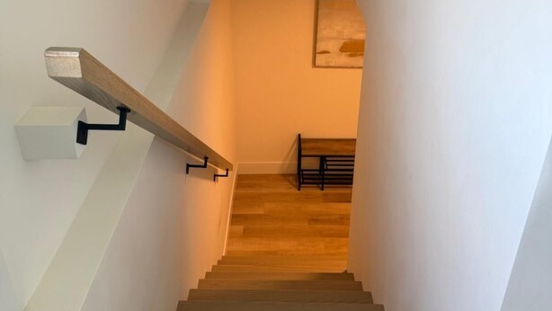 Una escalera con peldaños de madera y paredes blancas, que conduce a una habitación con suelo de madera y un banco.