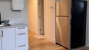 Una cocina moderna con armarios blancos, un refrigerador negro y suelo de madera.