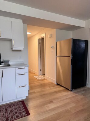 Cuina moderna amb armaris blancs, un refrigerador negre i un sòl de fusta.