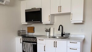 Una cocina moderna con armarios blancos, un microondas negro, un lavamanos de acero inoxidable y una alfombra estampada.